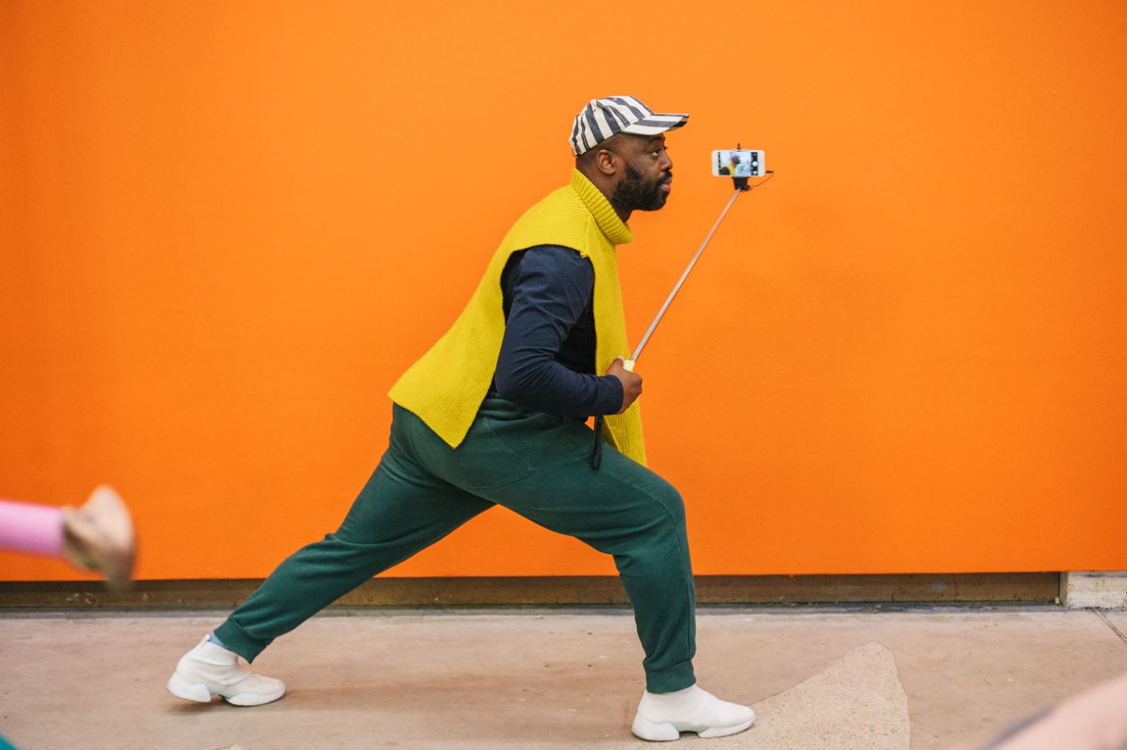 Man lunging infront of birght orange wall with selfie stick 